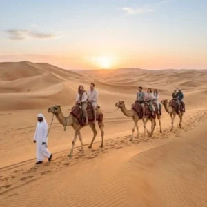 Tourists enjoying a camel ride during a Morning Desert Safari in Abu Dhabi at sunrise.